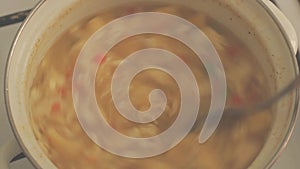 Top view, vegetable vegetarian soup boiling and cocked in a steel pan, stirring with a spoon. cooking steam. close up shot.