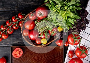 top view of vegetables as tomato green mint leaves basil in basket and cut tomato in tray on wooden background