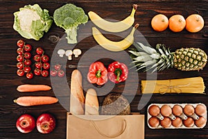 Top view of vegetables and fruits, bread and eggs on wooden table