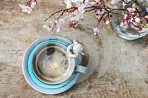 Top view of a vintage blue cup of coffee with an angel figurine and a vase with blooming tree branches on wooden background