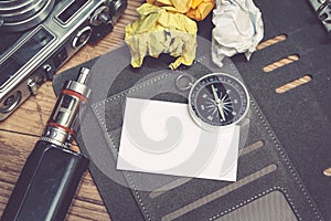 Top view of vintage camera, crumple paper,electronic cigarette and planner book layout on wooden floor.