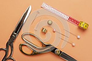 Top view of vintage scissors, pins, measuring tape and thimbles on the bright orange surface