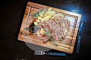 Top view of Wagyu beef steak set with the black pepper sauce and the potato and some vegetable on wooden board and black table