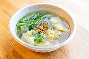 Top view of Wanton soup with morning glory and deep fried garlic in bio paper bowl on wooden background