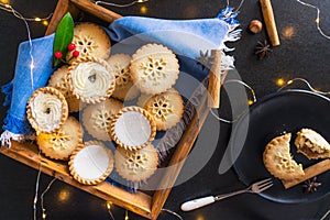 Top view warm cosy composition of traditional english festive pastry mince pies in wooden tray, spices, black plate with broken