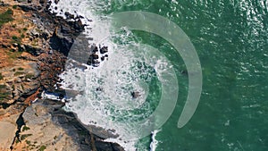 Top view waves barrelling to rugged coastal cliffs. Drone shot powerful ocean