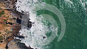 Top view waves barrelling to rugged coastal cliffs. Drone shot powerful ocean