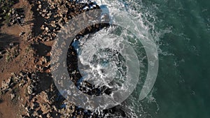 Top view waves break on rocks in a blue ocean. Aerial drone view of sea waves 4k shot. Bird's eye view of ocean waves