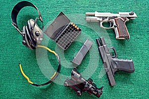 Top view weapons : Two pistols, Ear Muffs and bullets and Semi-automatic gun for self-defense on green table