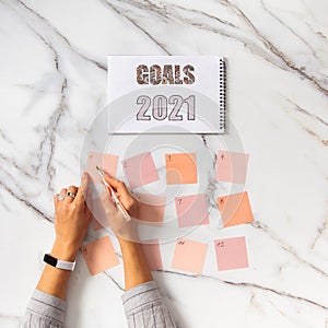 Top view of well groomed female hands near stack of colorful notepads for writing goals and plans