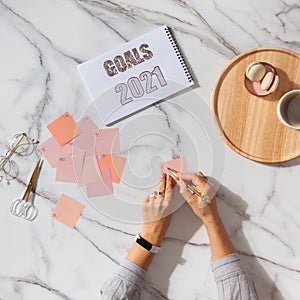 Top view of well groomed female hands near stack of colorful notepads for writing goals and plans. Marble background