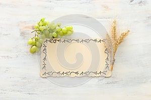 Top view of wheat crops and green grapes over white wooden background. Symbols of jewish holiday - Shavuot