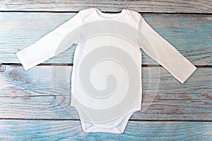 Top view white baby bodysuit with long sleeve on wooden background. Copy space for lettering or your text. Flat lay mockup. Stock