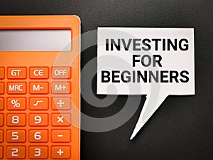 Top view white bubble speech written INVESTING FOR BEGINNERS with calculator isolated on black background.