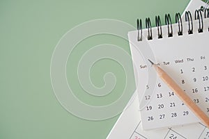 Top view of white calendar and sharpen brown pencil on green background, schedule, timeline, planning concept