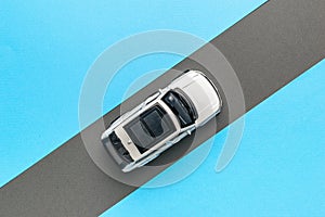 Top view of a white car moving along a gray road on a blue background. The concept of auto mania