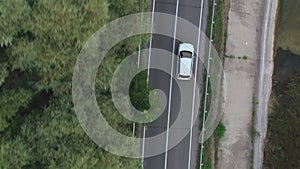 Top view of white car rides through dam route. SUV drives at road near lake on summer day. Flying over the auto moves