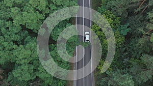 Top view of white car riding along road in green forest. Auto driving at rural route at summer day. SUV moving through