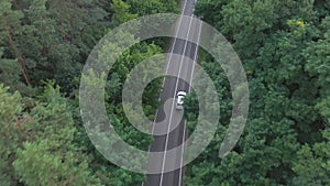 Top view of white car riding along road in green forest. Auto driving at rural route at summer day. SUV moving through