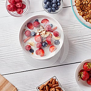 Ingredirnts for preparing healthy organic breakfast - granola, strawberries, honey, banana in white bowl with milk on