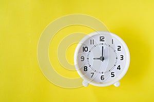Top view of white clock at nine o`clock on yellow background