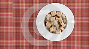 Top view of white coffee or tea cup full brown sugar cubes on red squared background. Diet unhealty sweet addiction photo