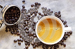 Top view of a white cup of black coffee with a pile of organic brown roasted coffee bean and coffee filter holder on a rustic