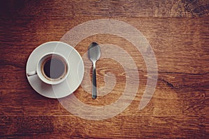 Top view of white Cup with black coffee on a white saucer and teaspoon on dark brown wooden background