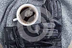 Top view of a white cup of coffee and black women`s gloves