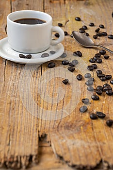 Top view of white cup of coffee, on rustic wooden table with coffee beans and spoon, selective focus