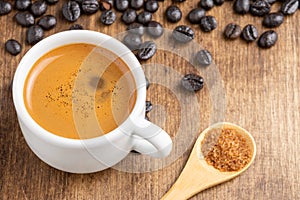 Top view of white cup with coffee on wooden table with coffee beans and wooden spoon with brown sugar,