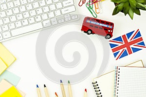 Top view white desk with blank spiral notepads, keyboard, British bus toy and Britsh flag. Foreign learning concept photo