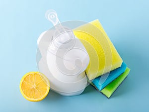 Top view on white dishwashing liquid in a plastic bottle, lemon and three foam sponges. Purity and household chemicals. Kitchen