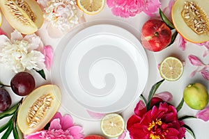 Top view of white empty plate, fruit and flowers. Flat lay, spring summer season holiday, femenine wedding table setting,