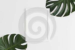 Top view of a white frame mockup with monstera leaf decoration. Portrait orientation