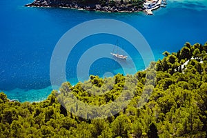 Top view of white lonely yacht in beautiful turquoise colored bay lagoon water surrounded by pine and cypress trees