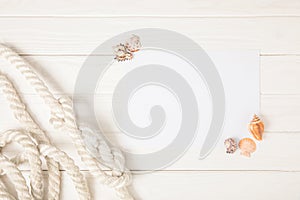 top view of white nautical knotted rope and empty paper with seashells on wooden surface