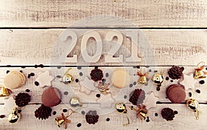 Top view of white number 2021, symbol of the coming New Year, macaroons and decorations on white rustic wooden background.