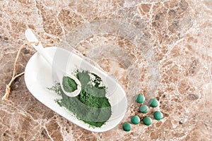 Top view of a white oval bowl with a white spoon filled with green organic spirulina powder. healthy supplements to promote health