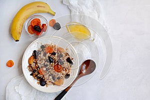 Top view of a white plate with rice porridge, dried fruits, bananas, honey on a light background. Layout, copy space