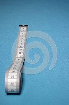 Top view of white soft measuring tape. Minimalist flat lay image of tape measure with metric scale over blue background.