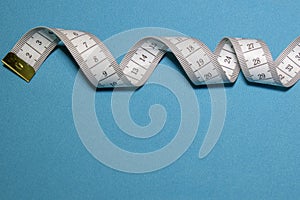 Top view of white soft measuring tape. Minimalist flat lay image of tape measure with metric scale over blue background.