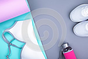 Top view of white sport shoes sneakers blue pink yoga mat, sport bra top, glass water bottle on pastel grey background