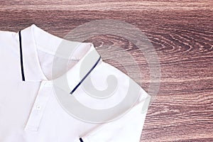 Top view of a white t-shirt with blue trim on a wooden background.