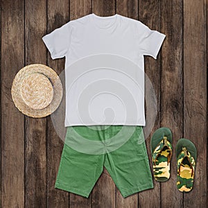 White t-shirt with green shorts, sandals, hat placed on the wooden floor