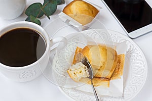 Top view of white table surface, cup of coffee, muffin on plate, smartphone, eucalyptus branch, styled image for social media