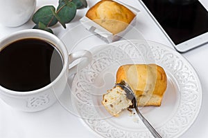 Top view of white table surface, cup of coffee, pastry on plate, smartphone, eucalyptus branch, styled image for social media, fem