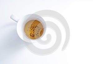 top view of a white tea cup on a white background with some tea infusion and tea grounds in the bottom of the cup, roiboos,