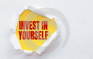 Top view of white torn paper and the text INVEST IN YOURSELF on a yellow background