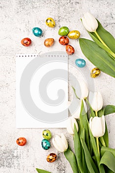 Top view of white tulips, blank calendar and colored easter eggs on concrete backgrund with copy space
